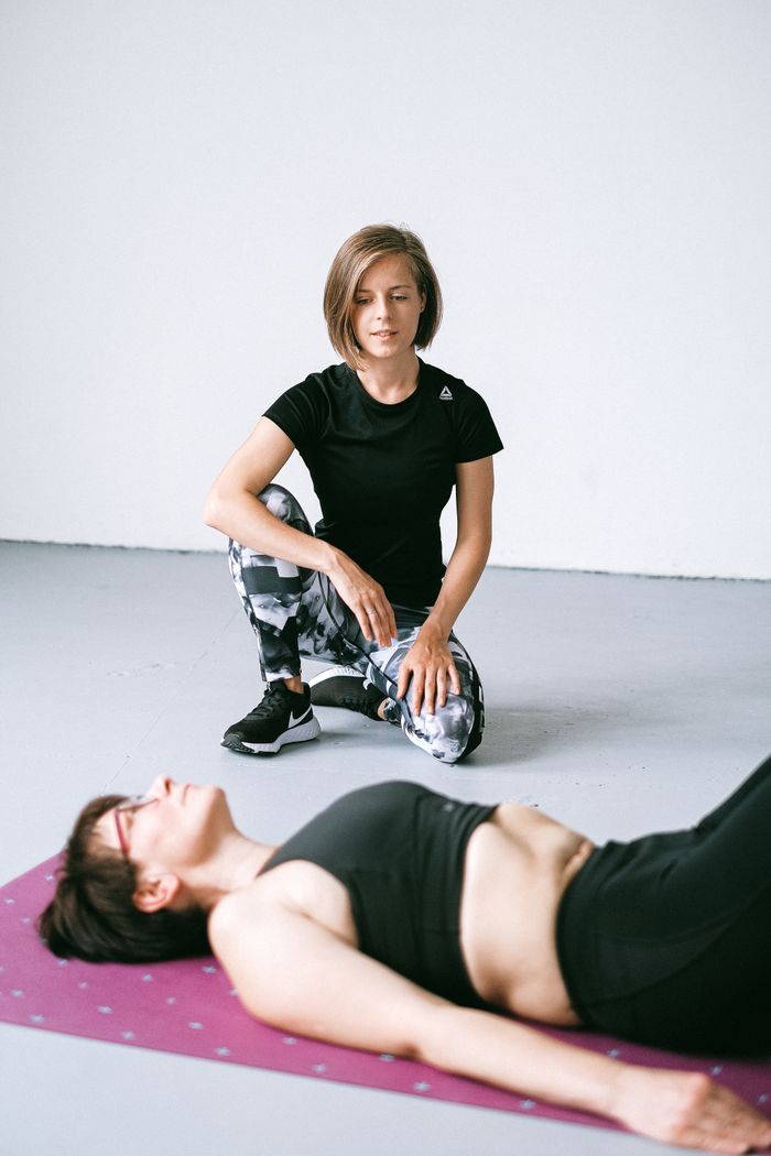 A personal trainer guides a client during an indoor exercise routine on a yoga mat.