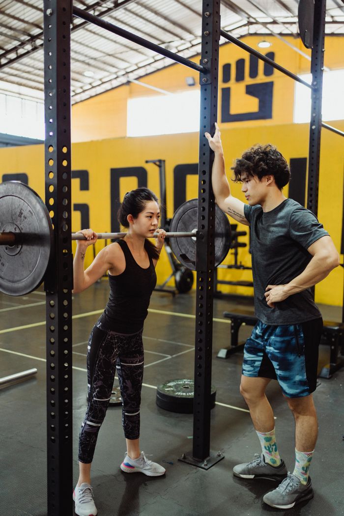 contact-img Asian couple working out in a gym, focusing on weightlifting and fitness training.